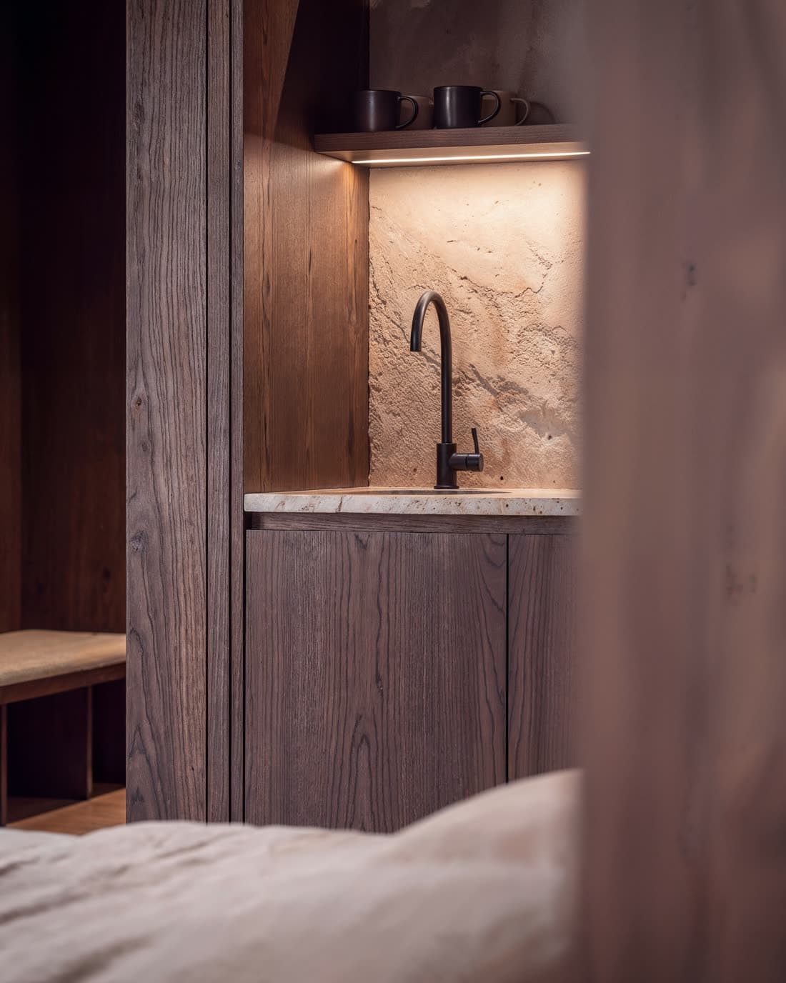The kitchenette counter, soft behind the end of the bed