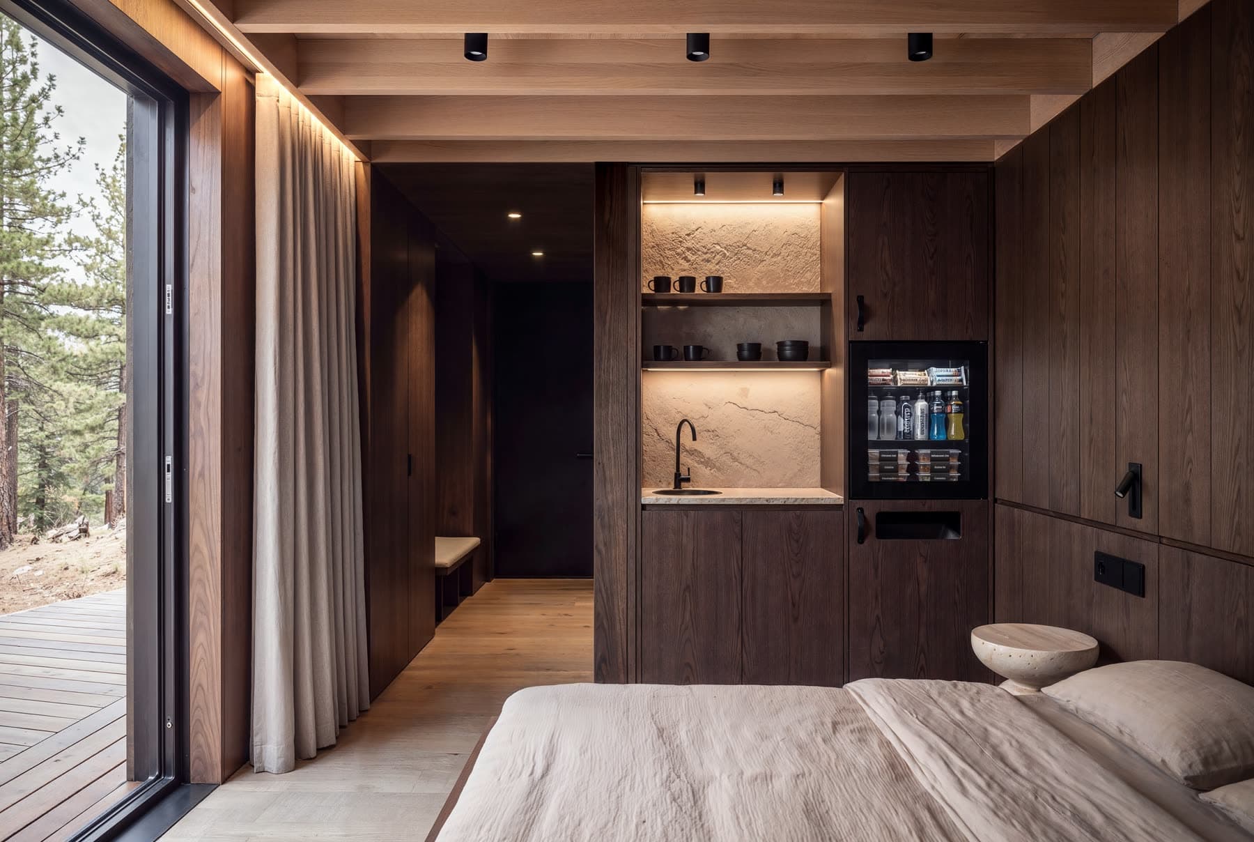 The kitchenette inside a cabin, with the glass door open to the deck and the trees beyond