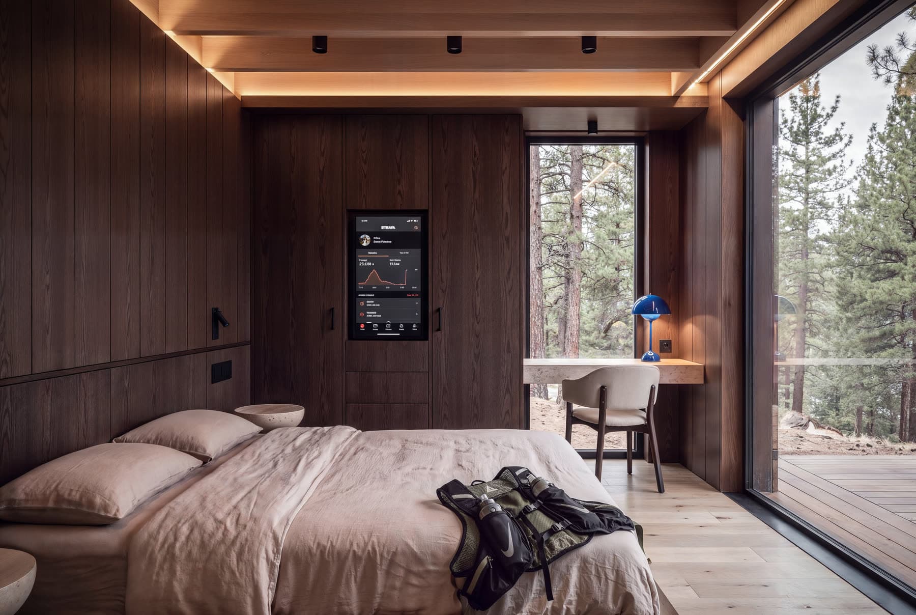 Inside a cabin: bed, desk, and a window wall onto the trees