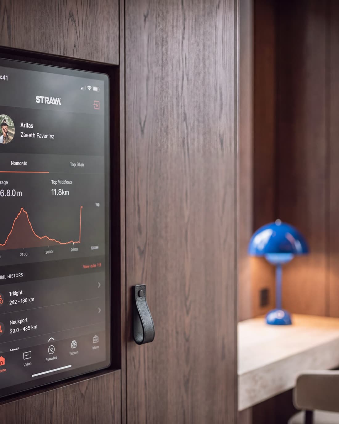A wall-mounted screen showing a run profile, beside a desk and reading lamp