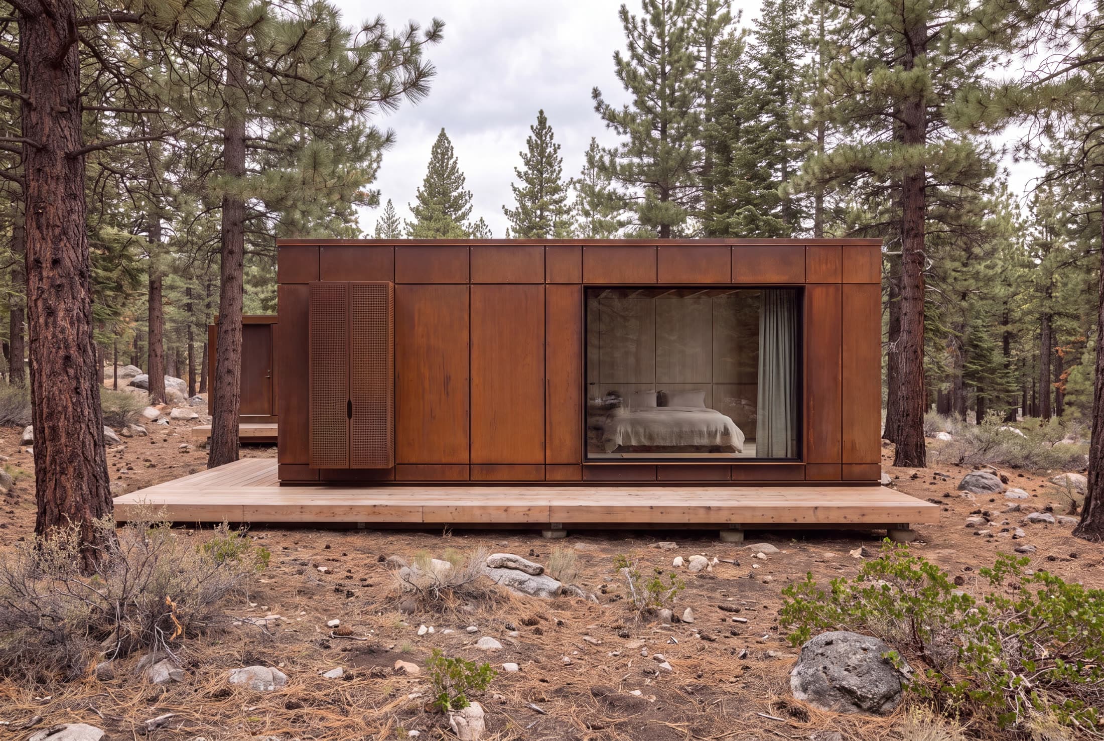 A single corten unit on a raised deck in the pines, bed visible through the glass wall